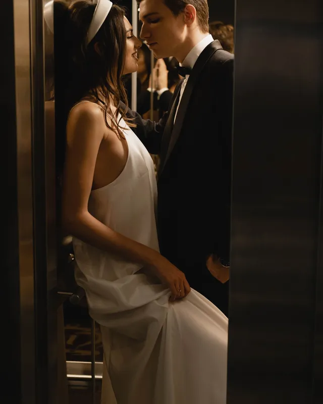 An elegant adult couple sharing a close kiss in a softly lit elevator.