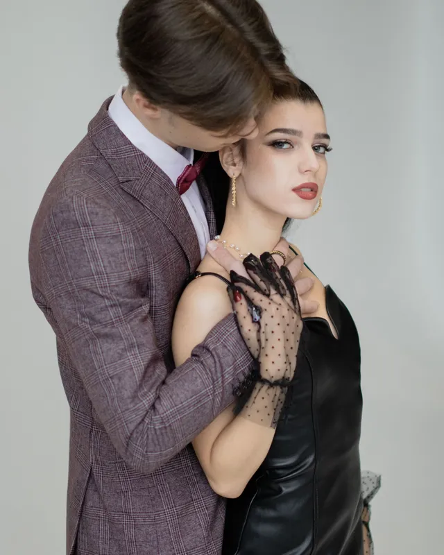 A stylish adult couple in eveningwear holding each other in a dramatic studio portrait.